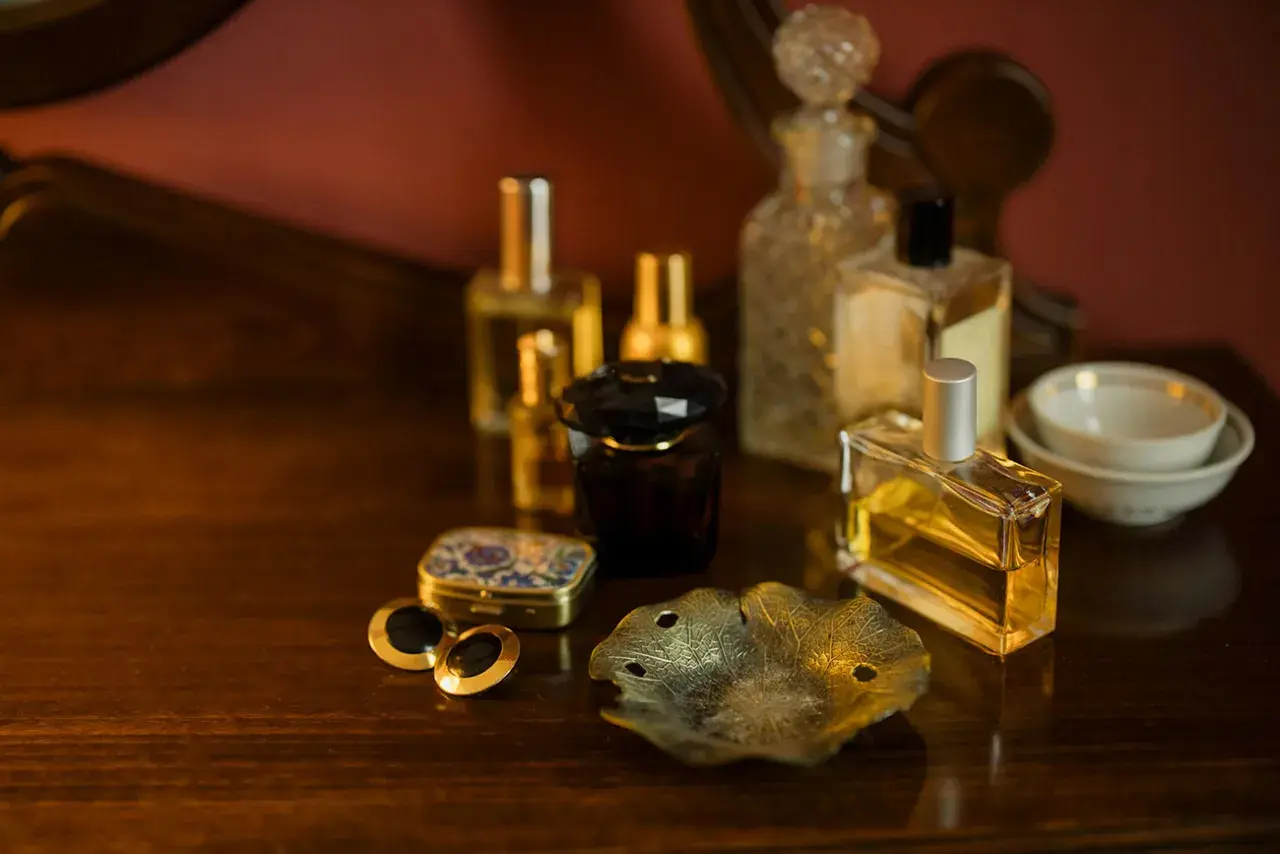 Eleganckie flakoniki z perfumami i woda kolońska co to? Na drewnianym blacie stoją różne rodzaje perfum, spinki do mankietów i ozdobna szkatułka.