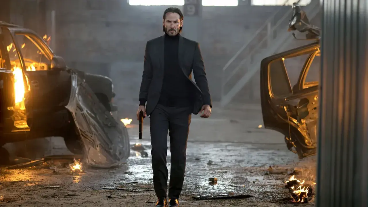 John Wick, med en pistol i handen, går genom ett inferno av brinnande bilar. En scen från rollistan i John Wick.
