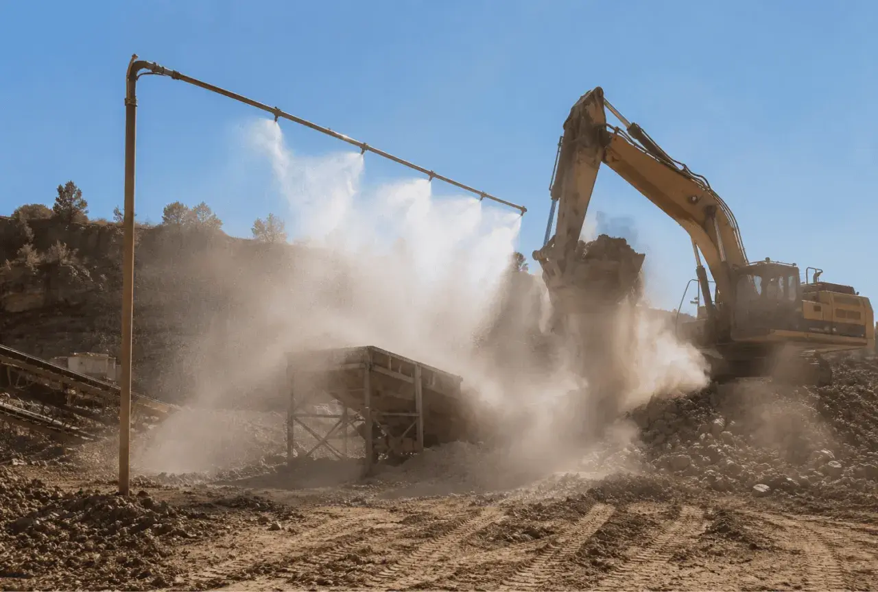 Excavadora amarilla trabajando en cantera, con sistema de desinfección por nebulización para controlar el polvo.