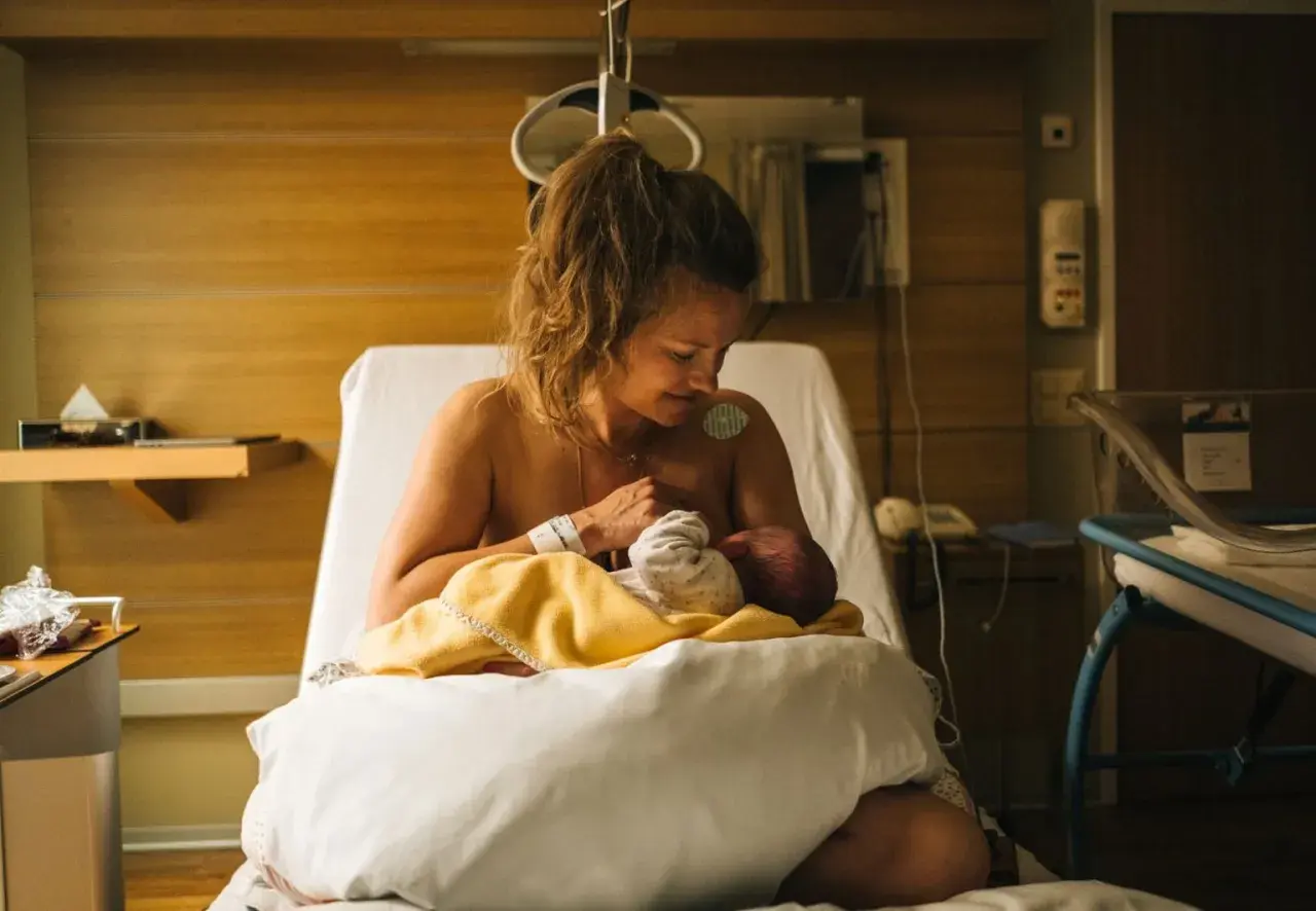Nybliven mamma ammar sitt barn på en sjukhussäng. En lugn stund efter förlossningen, kanske inför en efterkontroll på MVC.