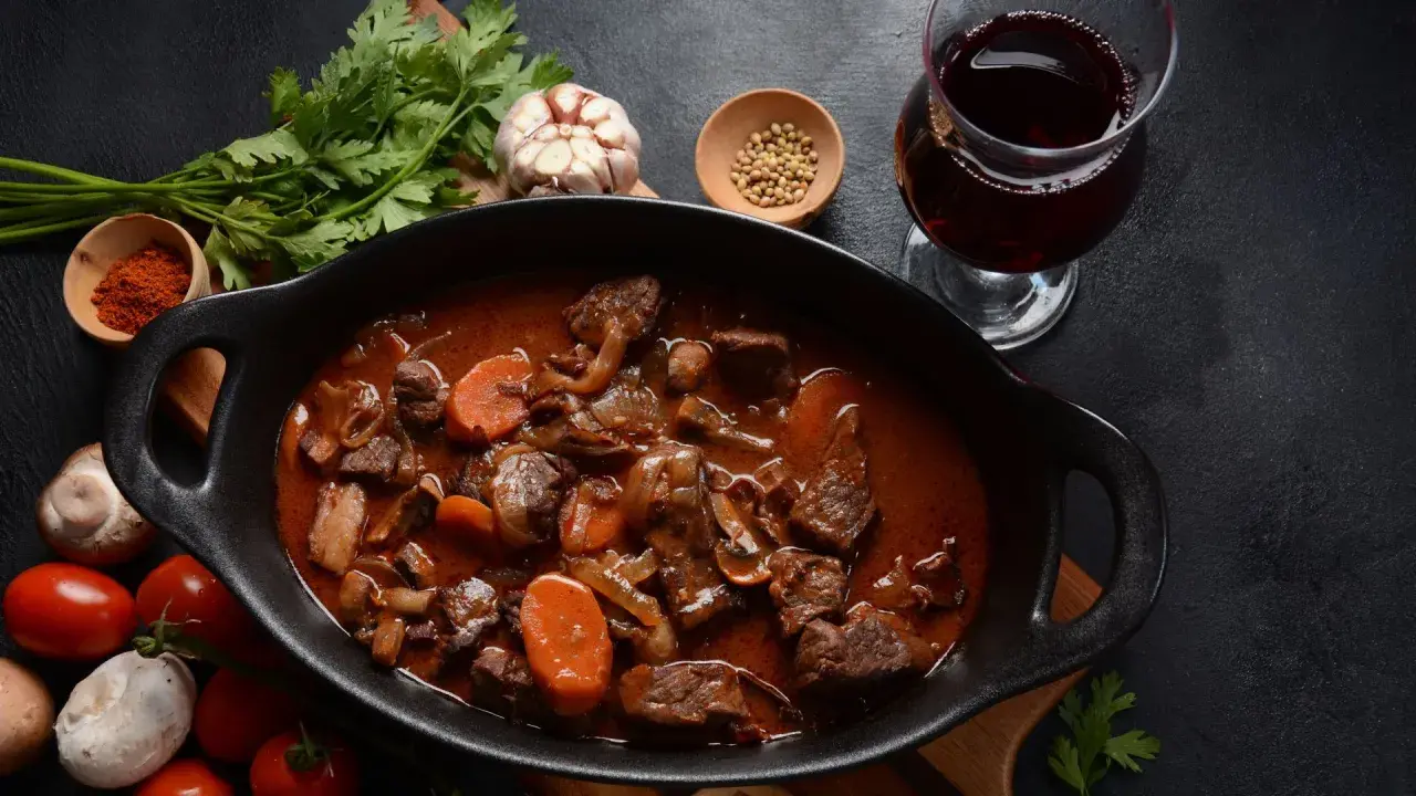 Un plat de bœuf bourguignon mijoté, avec carottes, champignons et oignons, accompagné d'un verre de vin pour bourguignon.