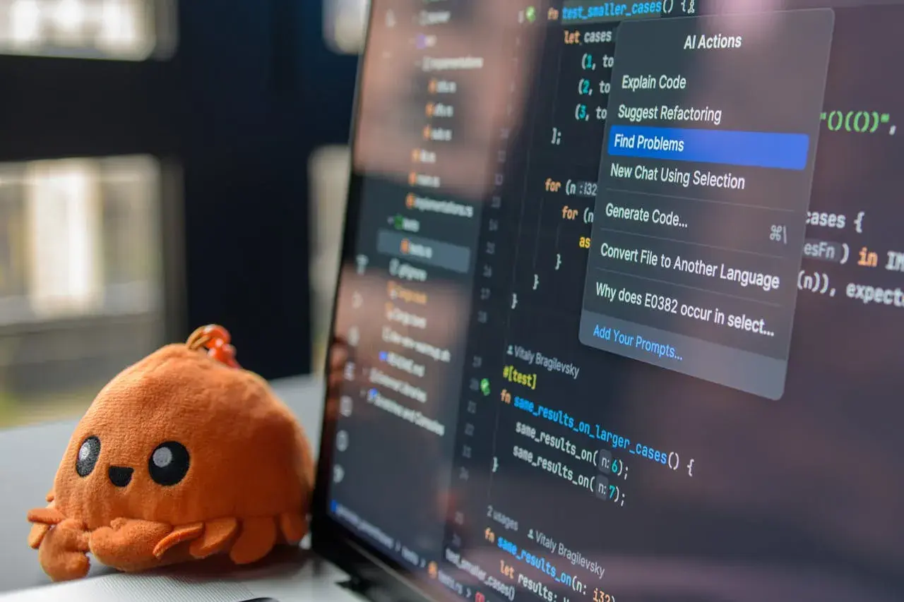 Un adorable crabe en peluche à côté d'un écran d'ordinateur affichant du code. Le menu contextuel propose des actions IA, aidant à choisir quel langage de programmation apprendre.