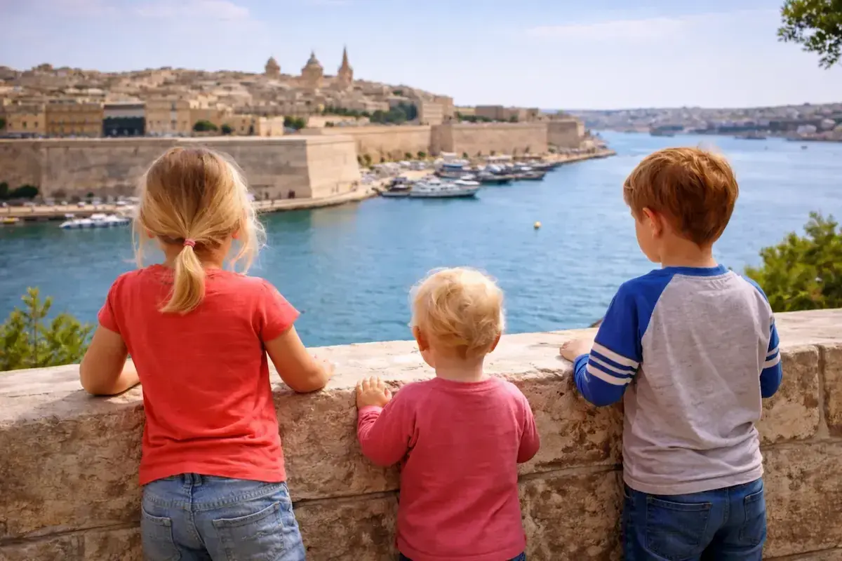 Drei Kinder blicken auf die Bucht von Valletta, Malta. Ein kleiner Junge, der fast wie ein Baby wirkt, steht in der Mitte.