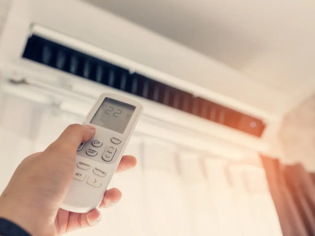 Mano sujetando control remoto de aire acondicionado para combatir el calor. La pantalla muestra 22 grados.