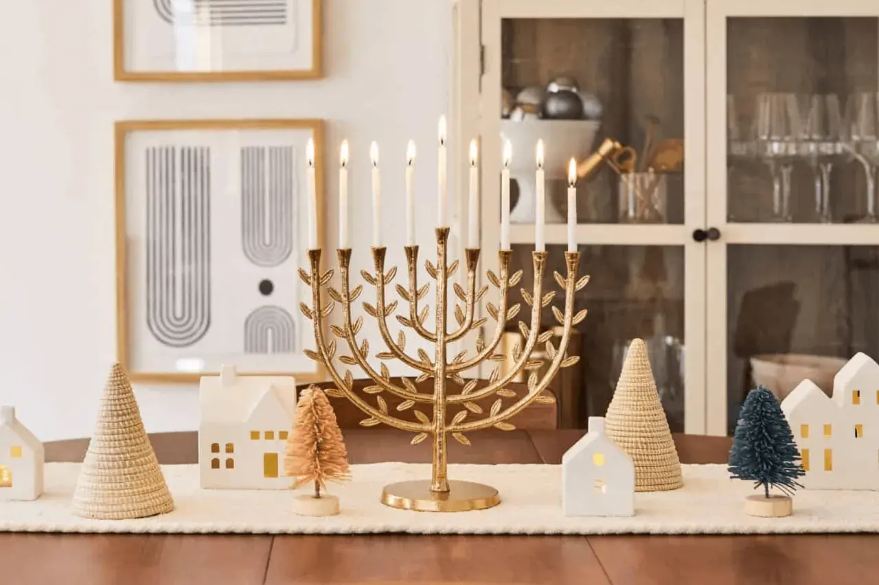 A golden menorah with lit candles is the centerpiece of this Chanukah decorating idea, surrounded by miniature houses and trees.