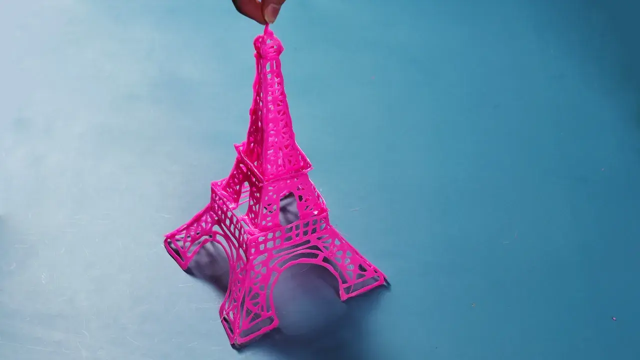 Una manualidad de la Torre Eiffel rosa, creada con filamento, sostenida por un dedo.