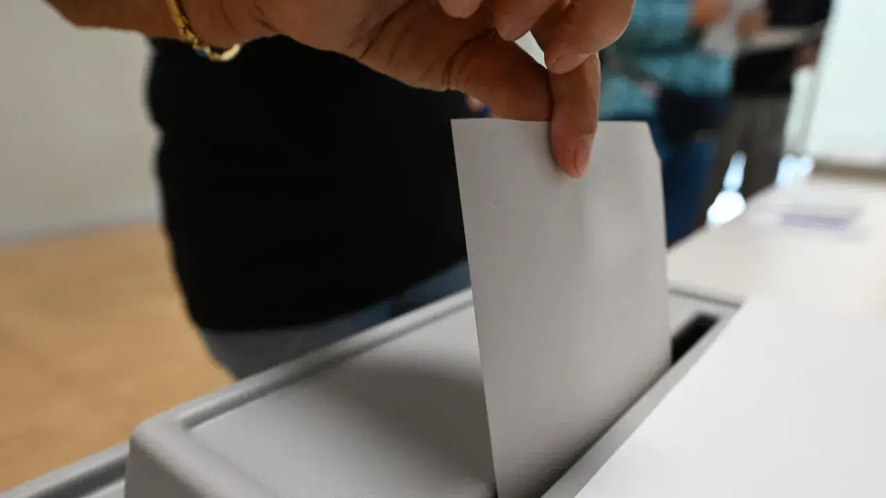 Hand wirft Stimmzettel in Wahlurne.