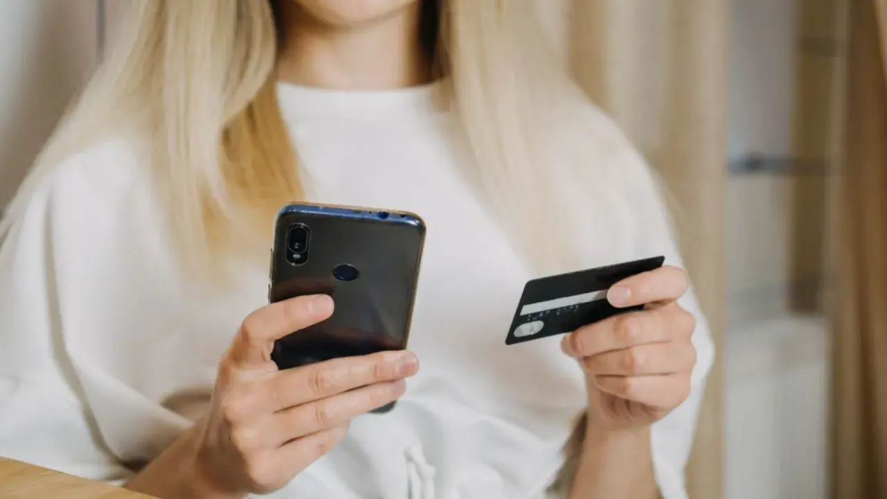Kobieta z blond włosami trzyma telefon i kartę płatniczą, szukając informacji, jak zwiekszyc limit PayPo.
