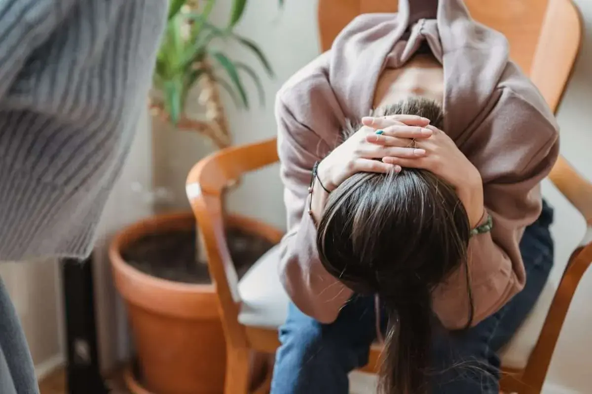 En person sitter med huvudet i händerna, ser ut att må dåligt. Kanske upplever hen biverkningar av något.