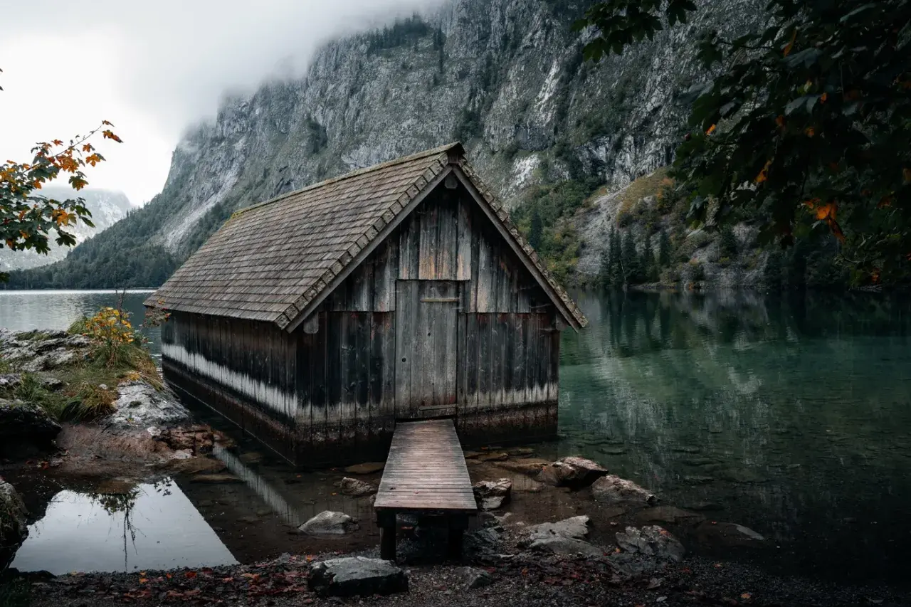Alte Holzhütte am Ufer des Obersee-Sees, umgeben von steilen Felswänden und nebliger Atmosphäre.