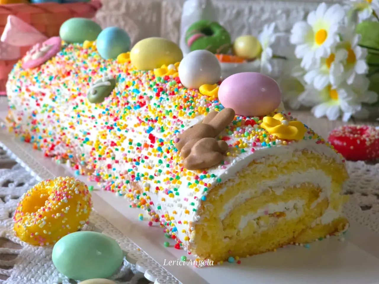 Bûche roulée décorée pour Pâques, recouverte d'un glaçage mascarpone facile et de vermicelles colorés, avec des œufs et un lapin en chocolat.