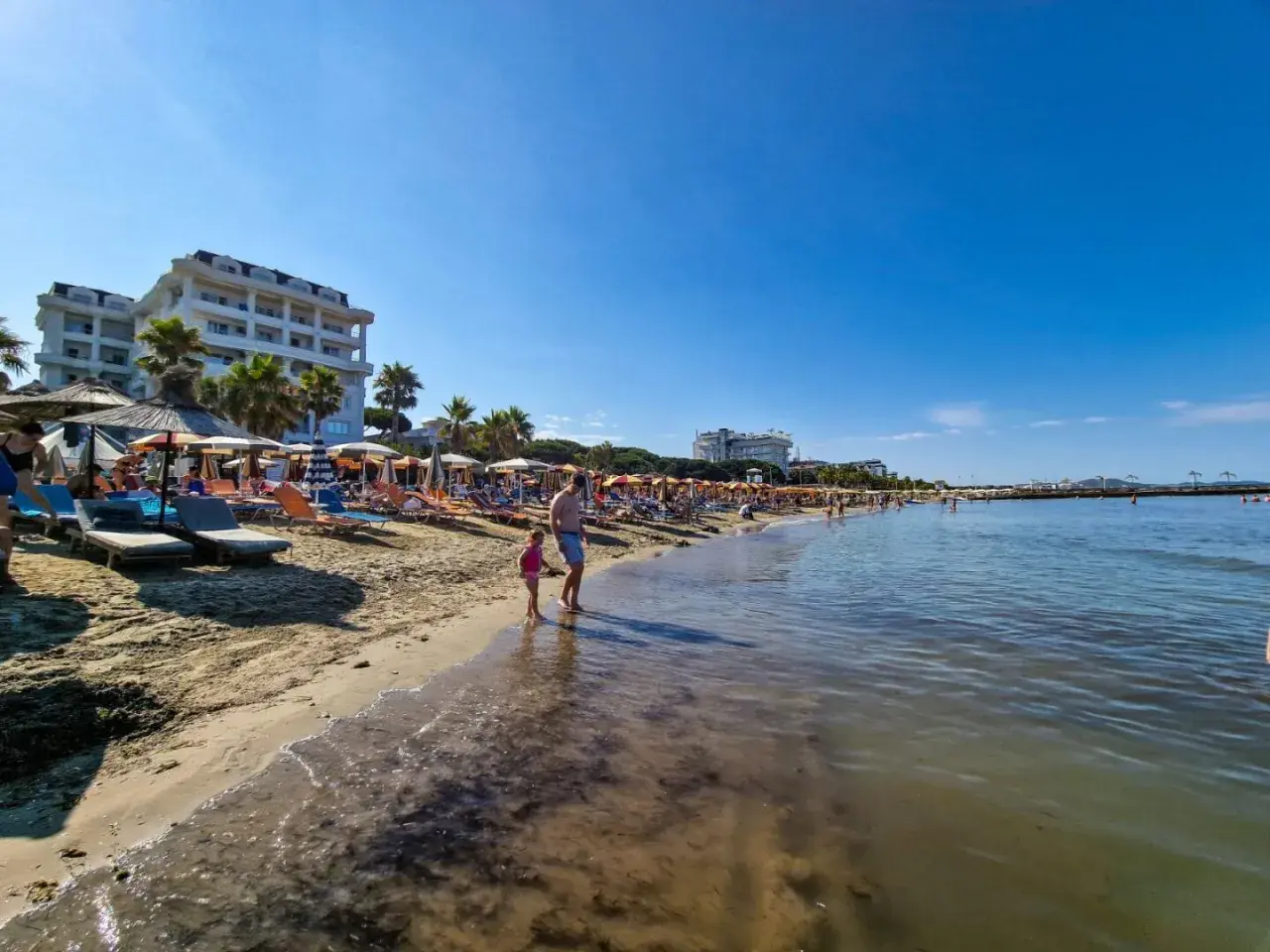 Słoneczna plaża w Golem, Albania, z leżakami, parasolami i hotelami. Idealne miejsce na wakacje, jedna z głównych atrakcji.