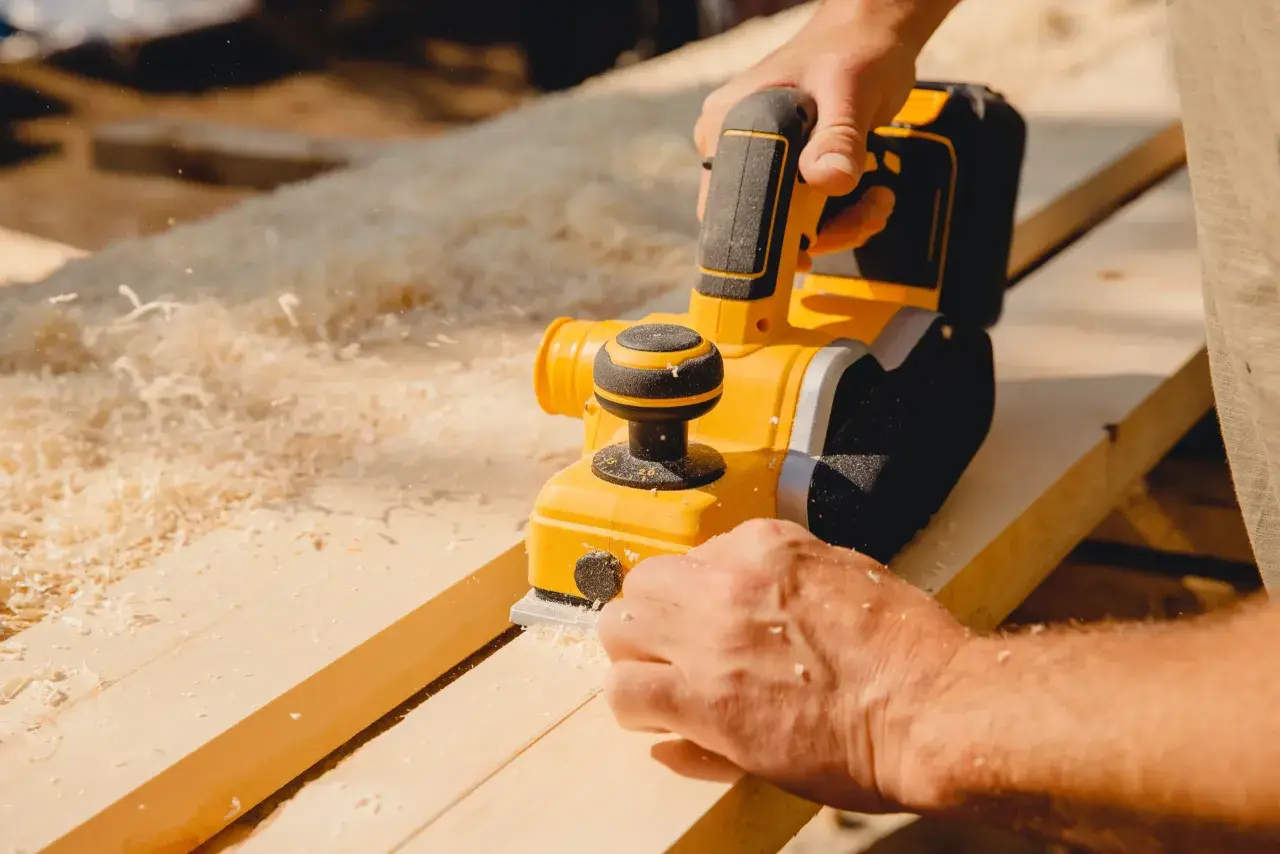 Un artisan utilise une raboteuse électrique pour raboter une porte en bois, produisant des copeaux fins.