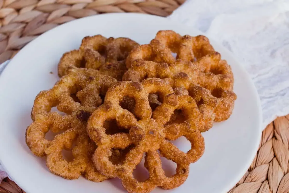 Un plato blanco con varios buñuelos de viento espolvoreados con canela y azúcar.