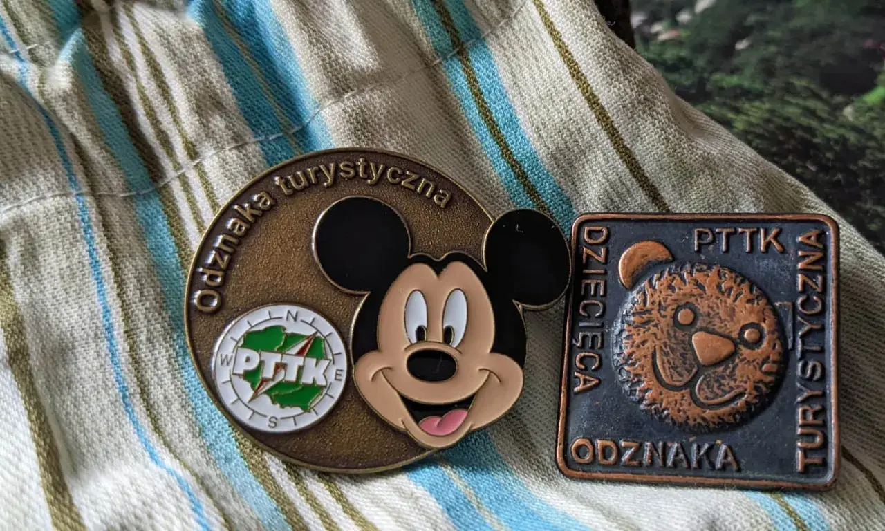 Dwie odznaki turystyczne PTTK: okrągła z Myszką Miki i kwadratowa z misiem.