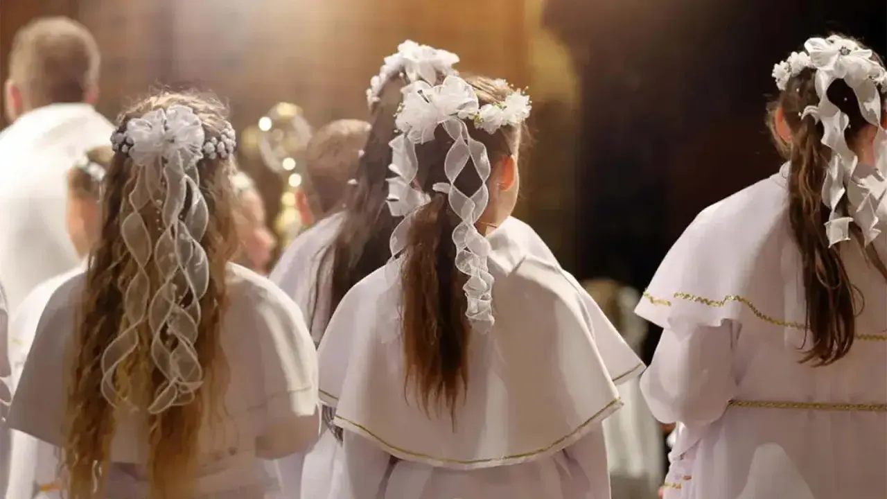 Dzieci w białych strojach, z wiankami na głowach, czekają na moment, kiedy jest komunia.