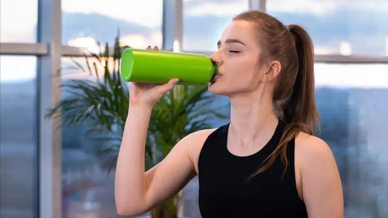 Junge Frau trinkt aus grüner Flasche. Sie fragt sich, wie viel Elektrolyte am Tag sie braucht, um fit zu bleiben.