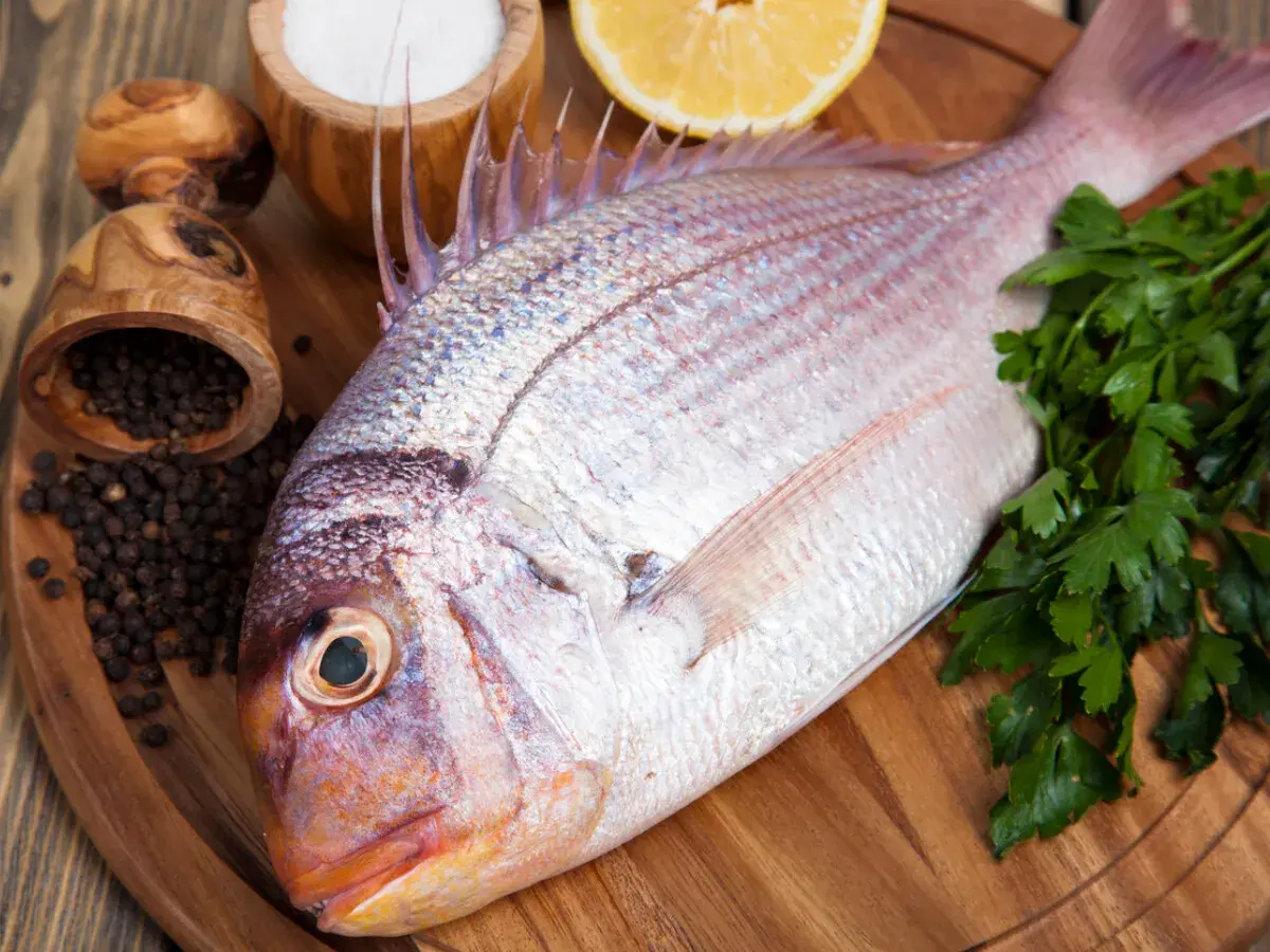 Un pescado rojo, listo para cocinar con perejil, limón, sal y pimienta negra.