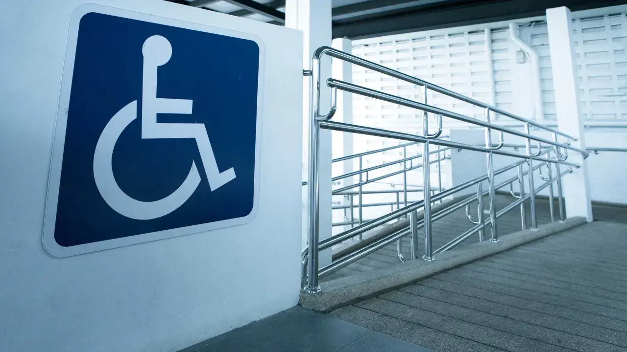 Segnale di accessibilità per disabili accanto a una rampa con corrimano, a norma con la legge 104 per l'abbattimento barriere architettoniche.