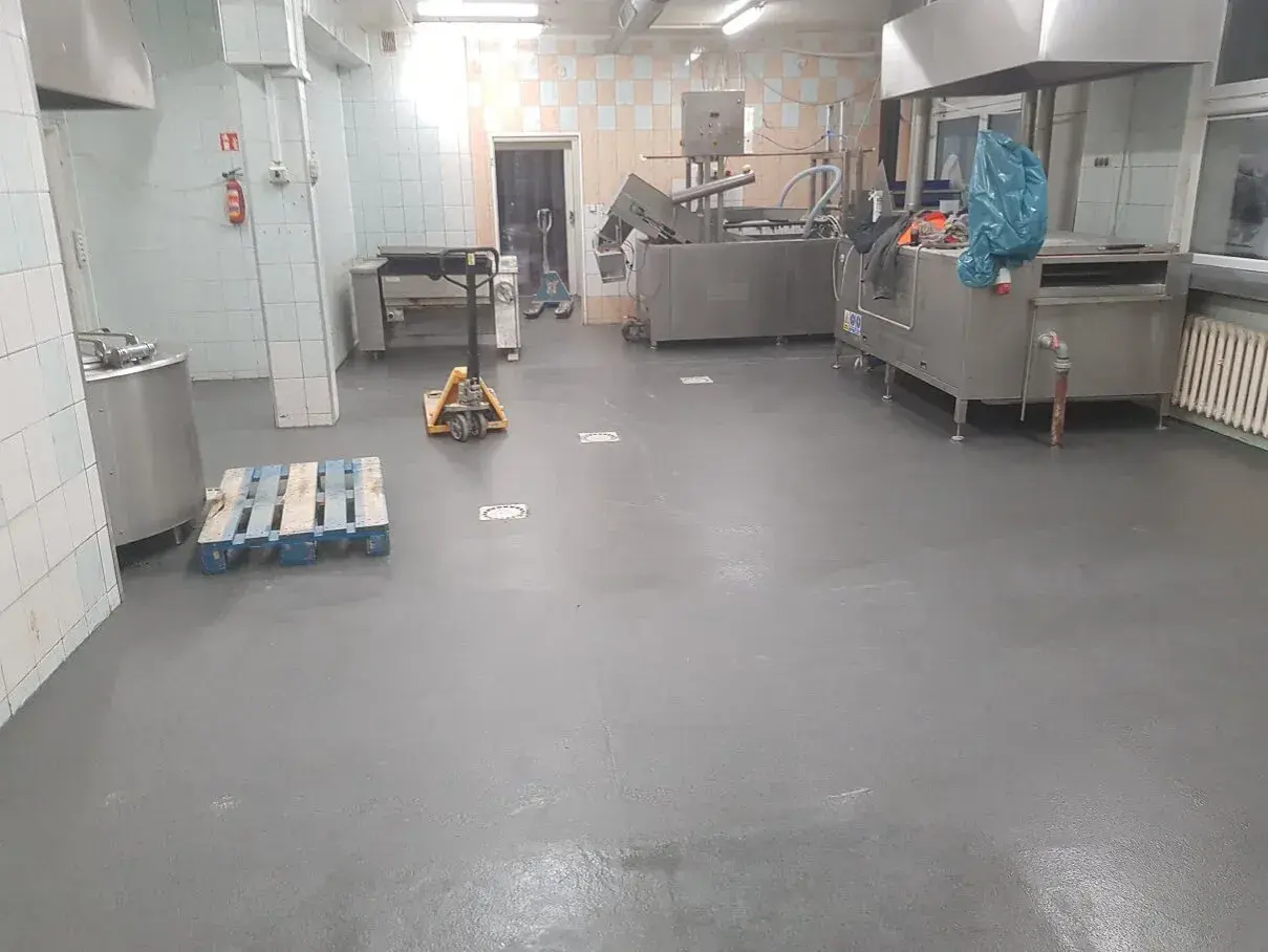 Nowa, szara wylewka betonowa w kuchni przemysłowej schnie, czekając na dalsze prace.