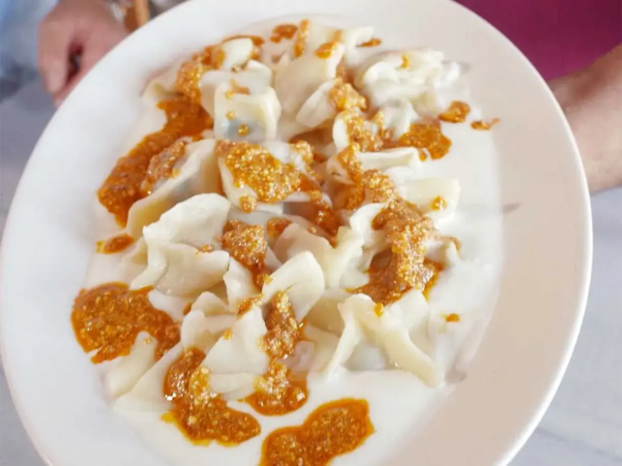 En tallrik med manti, små dumplings i en krämig sås med en kryddig topping. Perfekt för ett manti recept.