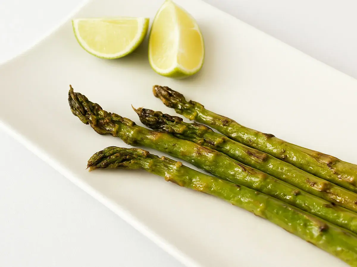 Asperges rôties sur une assiette blanche avec des quartiers de citron vert. Une idée simple pour une recette d'asperges savoureuse.