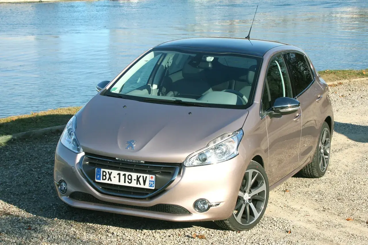 Peugeot 208 GPL color bronzo, parcheggiata su ghiaia vicino a un lago.