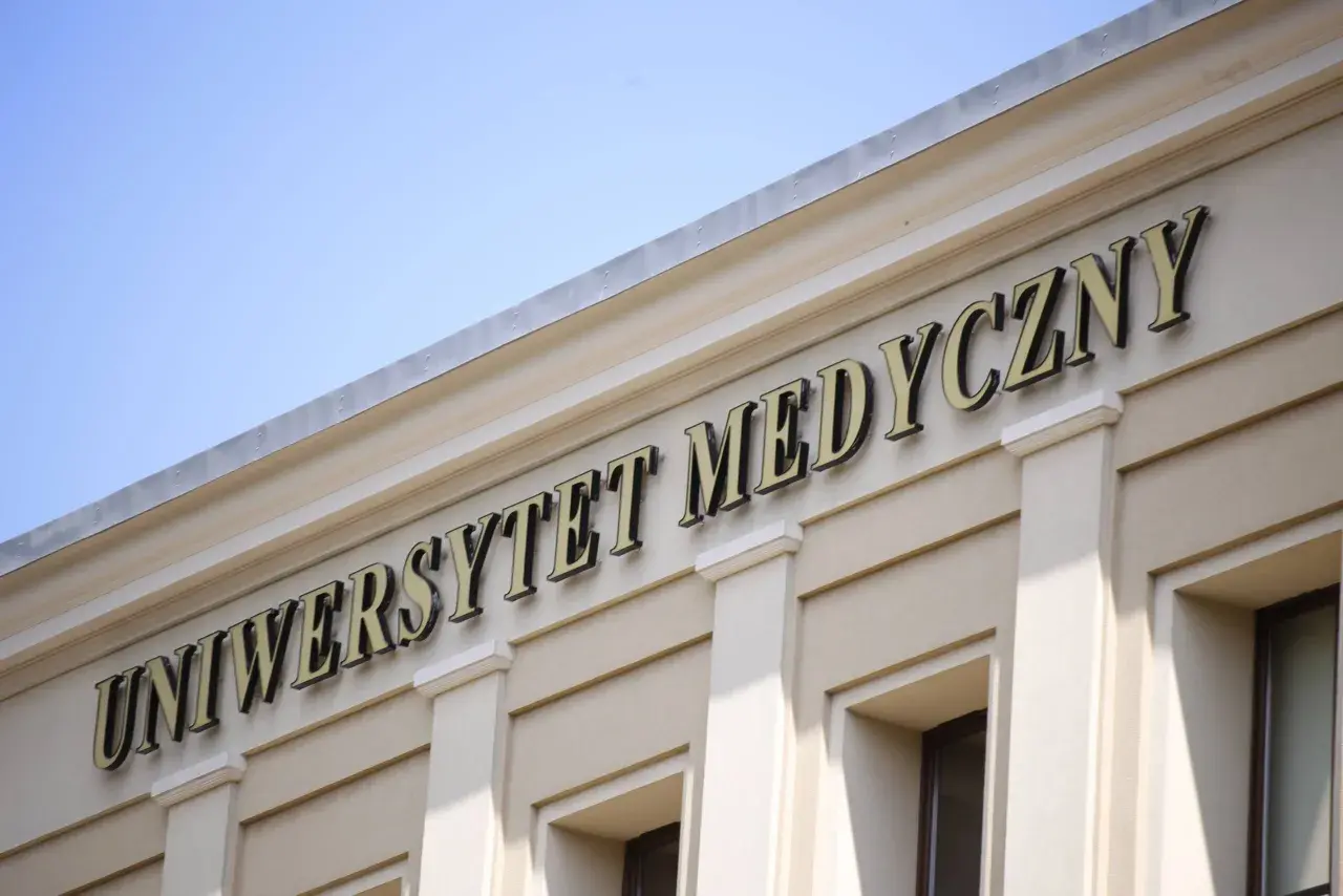 Napis "Uniwersytet Medyczny" na jasnej fasadzie budynku pod błękitnym niebem.