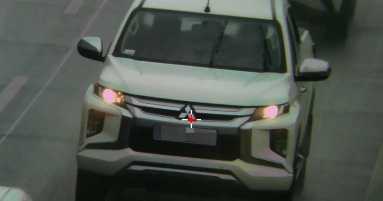 Biały pickup jedzie zderzakiem do przodu, z czerwonym krzyżem na grillu.