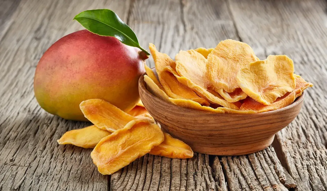 Un mango fresco e una ciotola di mango disidratato, che ne esaltano le proprietà nutritive e il sapore concentrato.