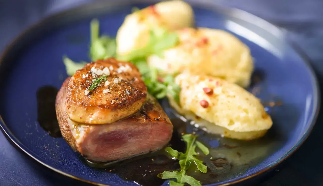 Tournedos de canard cuisson parfaite, garni de foie gras poêlé, servi avec une purée de pommes de terre et des roquettes.