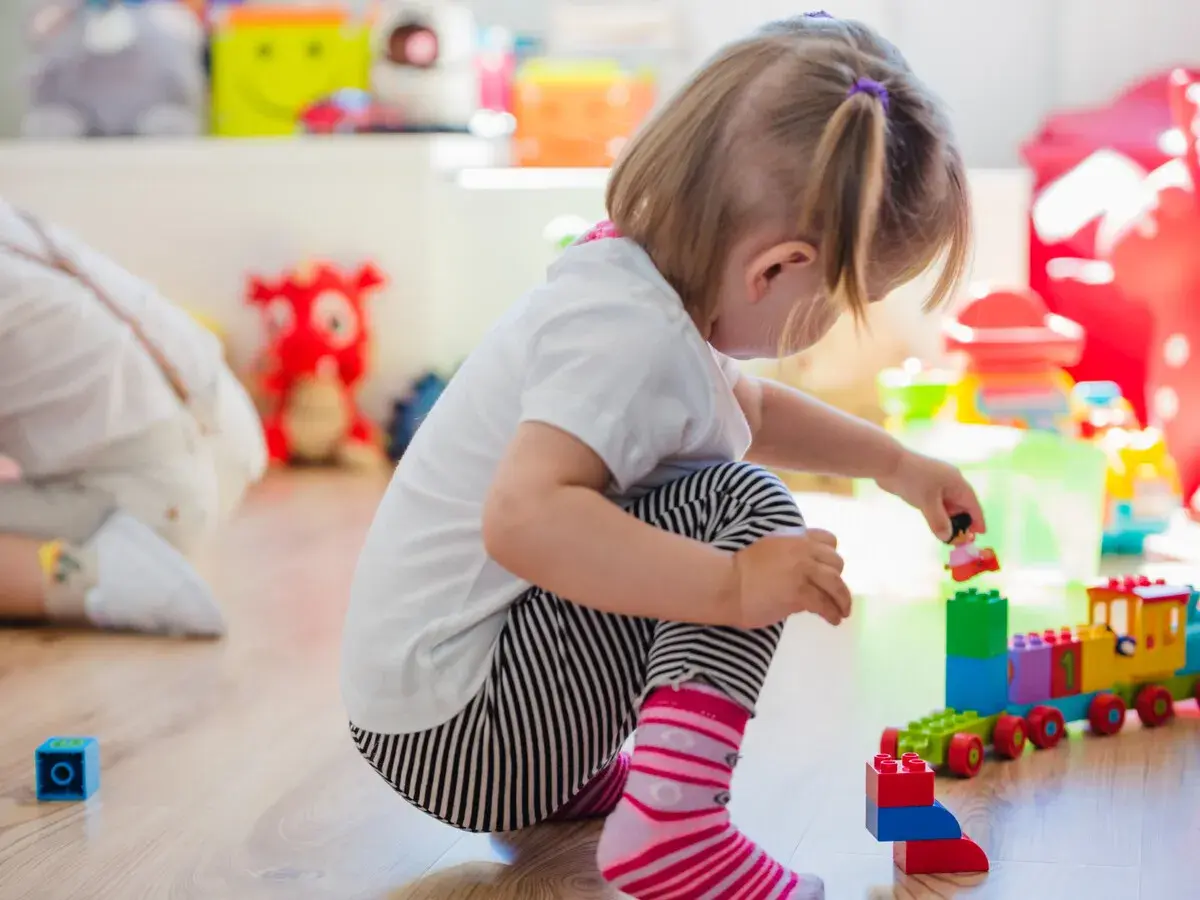 Niña de 0-3 años jugando con bloques de construcción. Crea un tren de juguete y una figura humana.