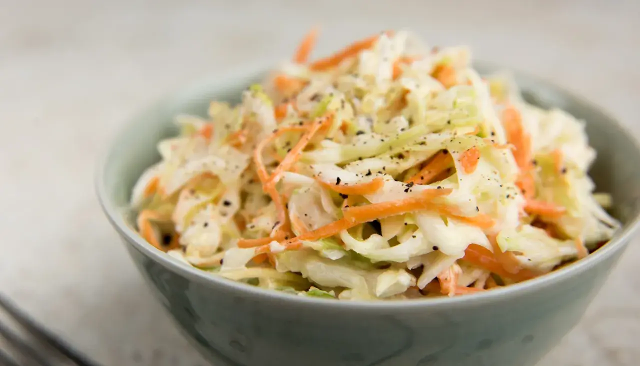 En skål med krämig, krispig coleslaw med strimlad vitkål och morötter, toppad med svartpeppar. Perfekt som tillbehör till grillat, detta är den godaste coleslaw!