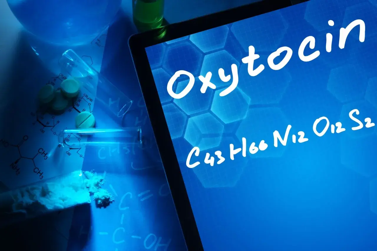 Badania nad oksytocyną u mężczyzn. Na ekranie tabletu widnieje nazwa "Oxytocin" i jej wzór chemiczny. Wokół leżą tabletki, proszek i probówki.