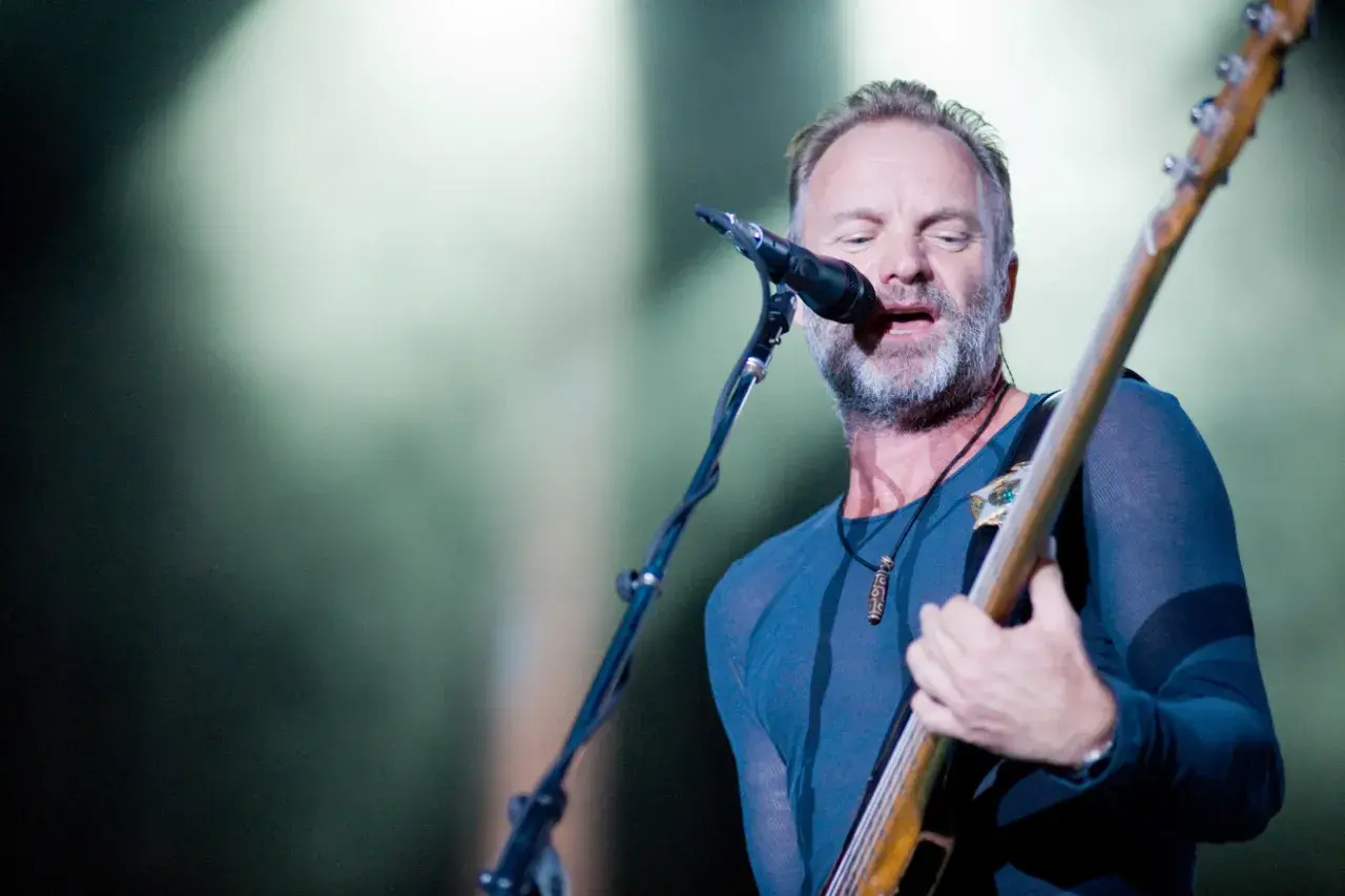 Sting, wokalista The Police, gra na gitarze basowej i śpiewa do mikrofonu na koncercie.