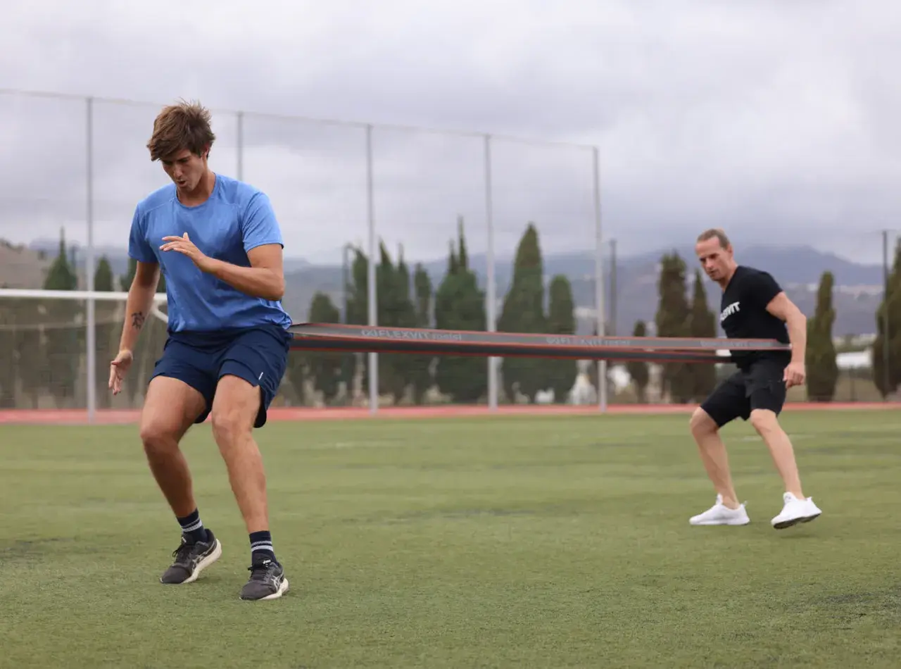 Zwei Männer trainieren auf einem Fußballfeld mit einem Widerstandsband für einen explosiven sprint.