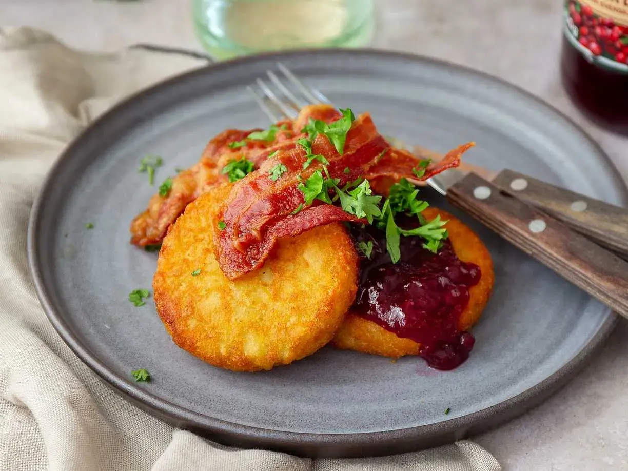 Gylla potatisbullar airfryer med knaprigt bacon, lingonsylt och persilja på en grå tallrik. En klassisk svensk rätt.