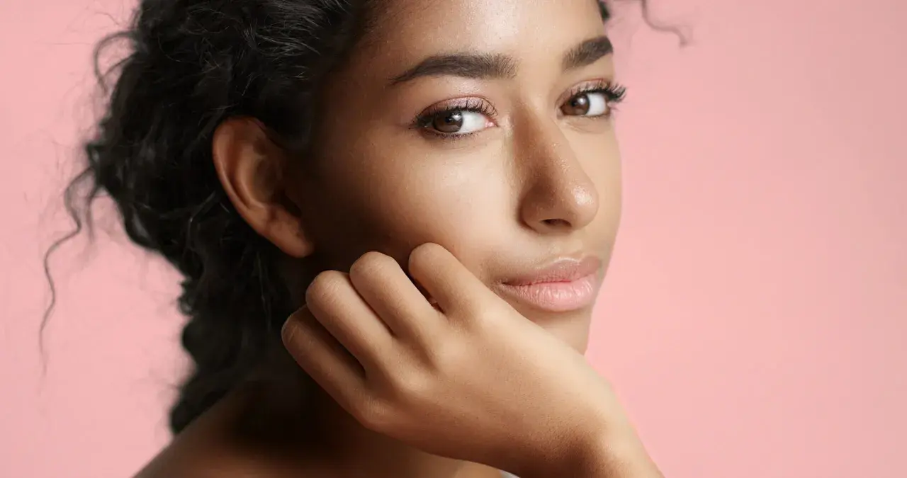 Portrait d'une jeune femme à la peau de couleur de peau olive, aux cheveux sombres et bouclés, posant sa main sur sa joue.