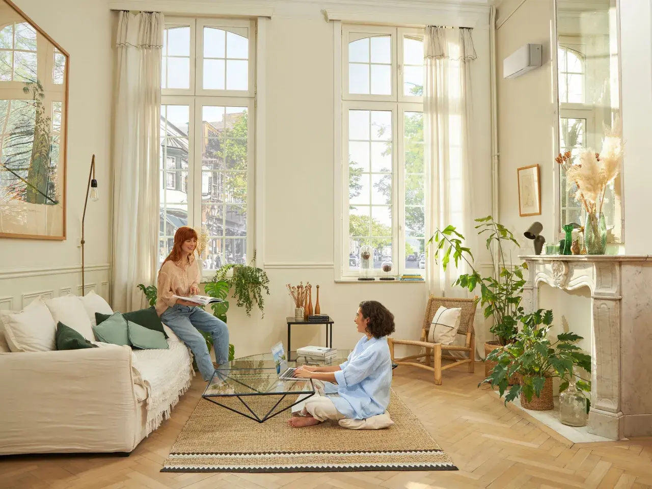 Dos mujeres disfrutan de un ambiente confortable en un salón luminoso, con el aire acondicionado en modo quiet funcionando discretamente.