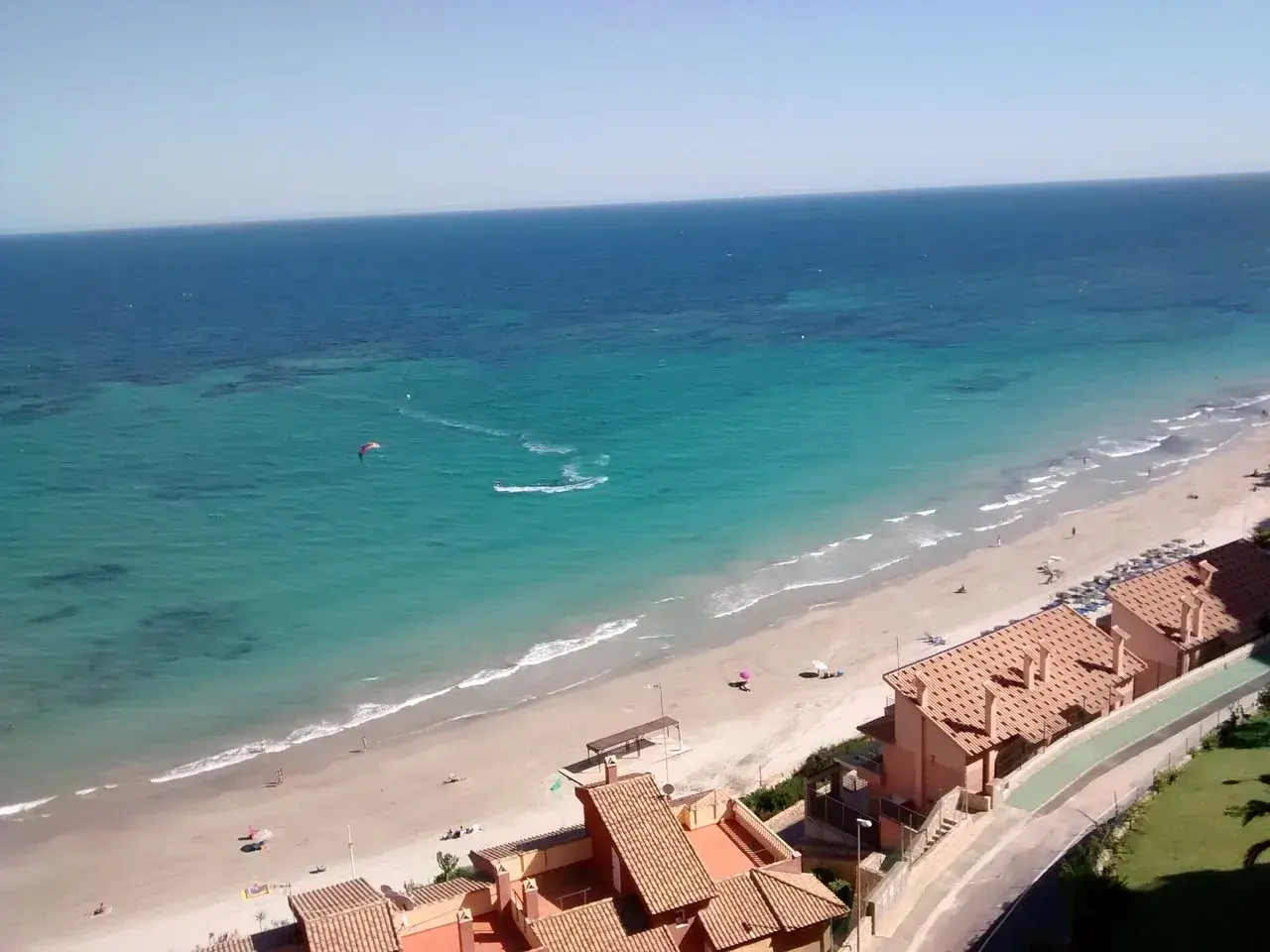 Vista aérea de la Campoamor playa con aguas turquesas, gente disfrutando del sol y un kitesurfista en acción.