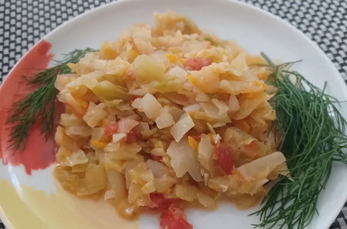 Młoda kapusta z pomidorami, duszona z koperkiem, na białym talerzu.