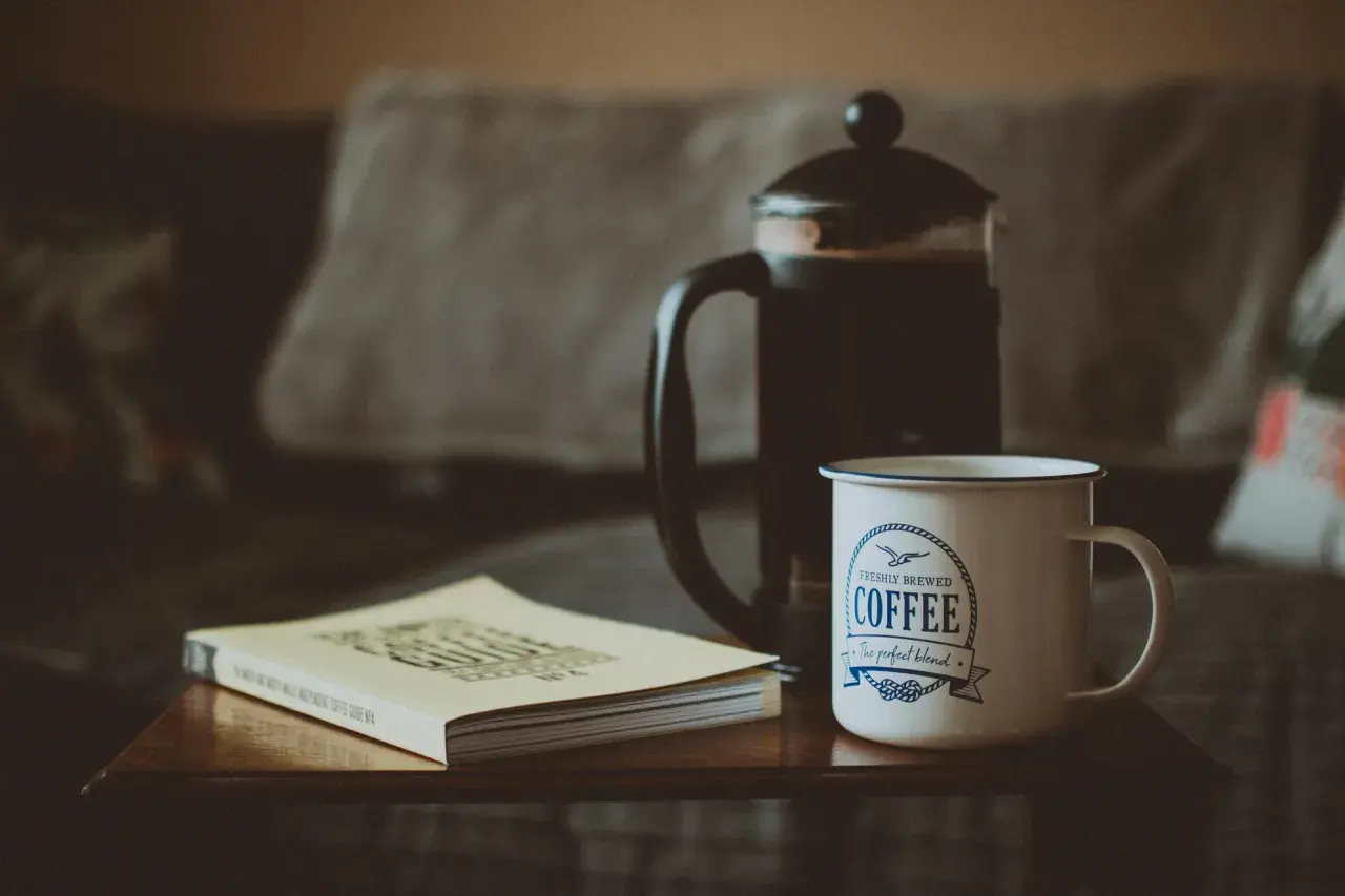 French press z kawą, kubek z napisem "Coffee" i książka o kawie. Idealny zestaw, by dowiedzieć się, ile kawy do french press.