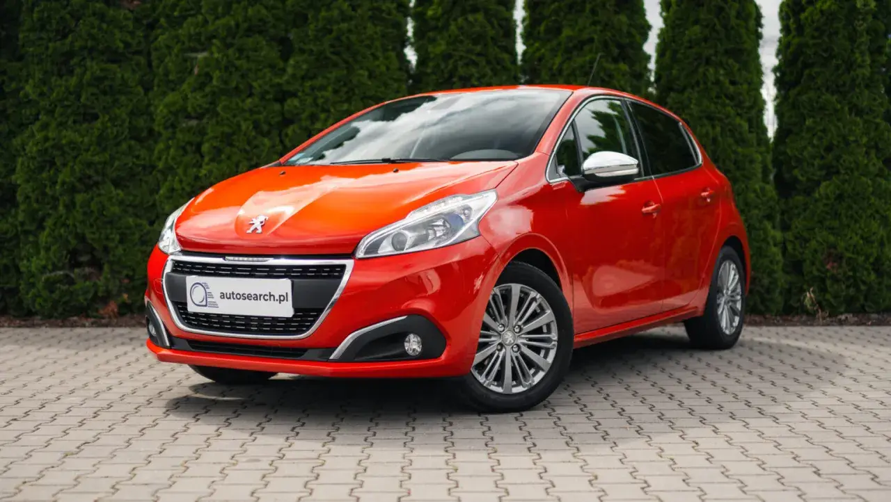 Czerwony Peugeot 208 z błyszczącymi światłami, idealny na egzamin na prawo jazdy.
