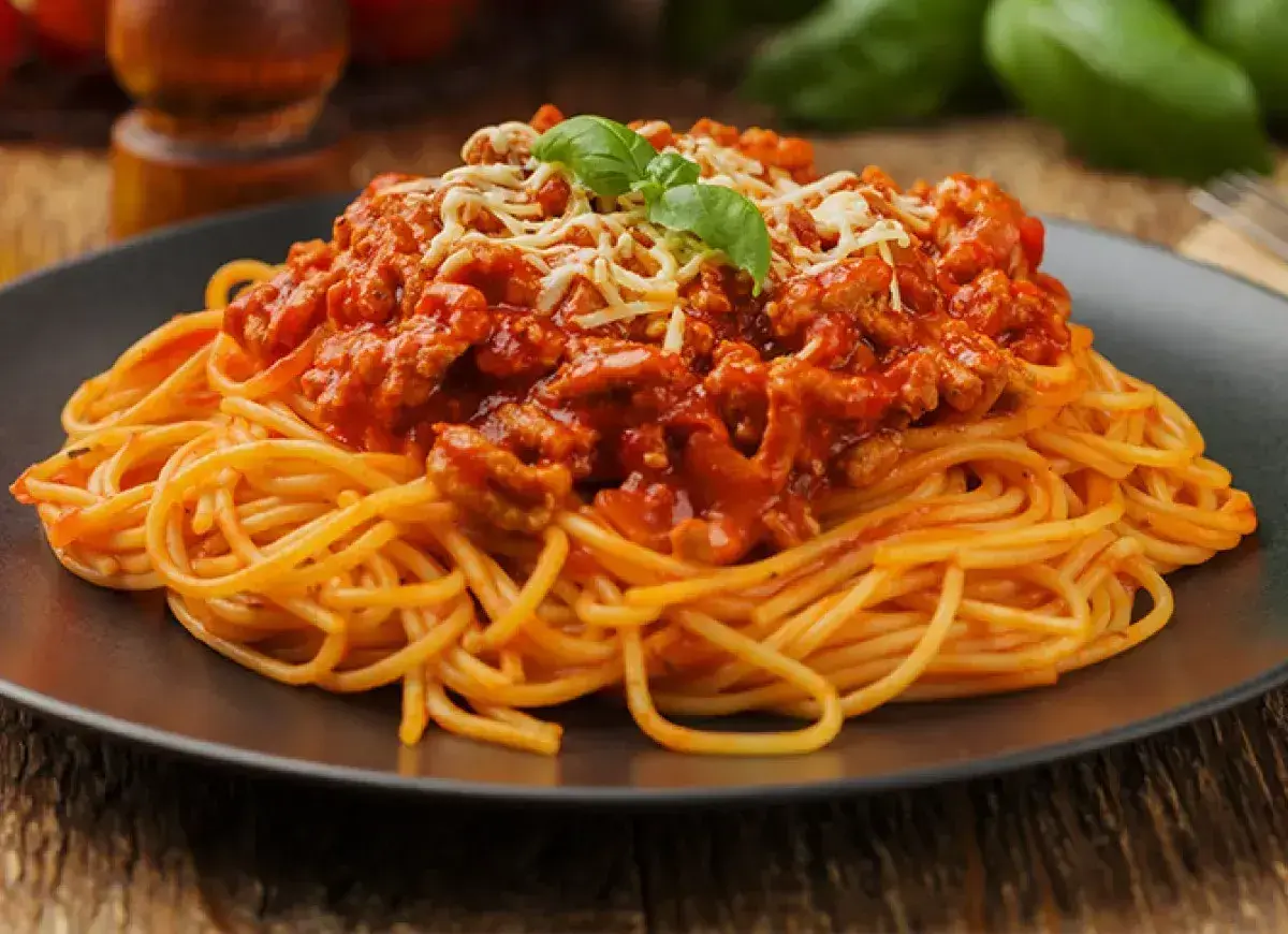 Porcja spaghetti z bogatym, mięsnym sosem bolognese, posypana startym serem i listkiem bazylii.