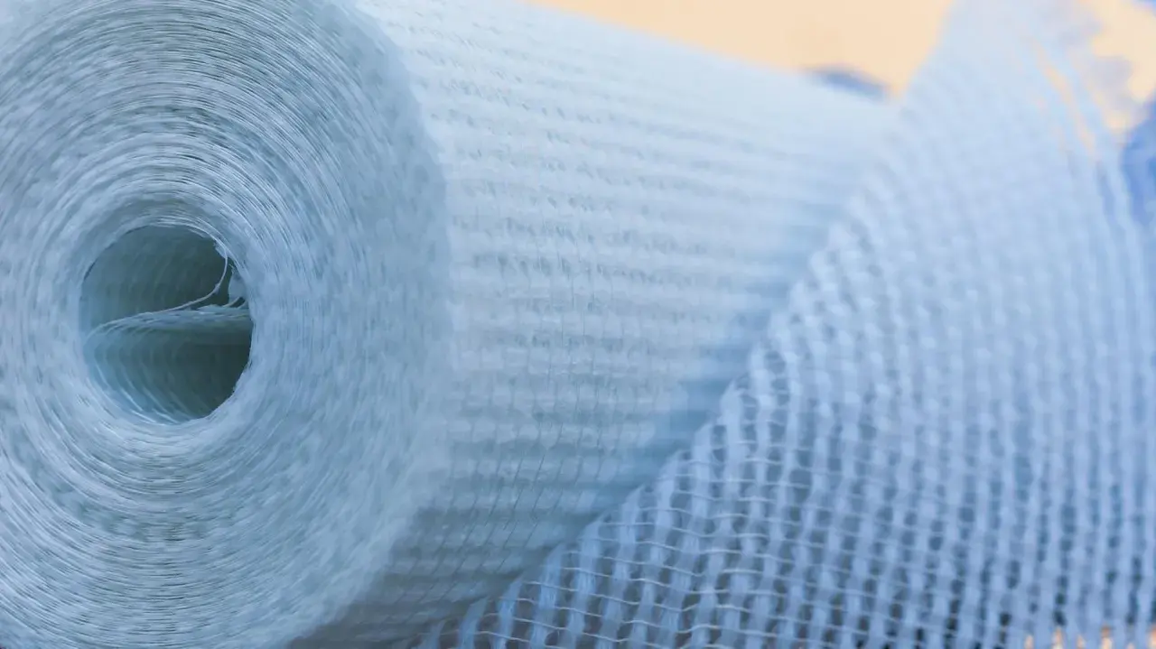Rolle aus Glasfasergewebe, bereit zum Glasfasertapete kleben. Das Material ist hellblau und hat eine feine Netzstruktur.