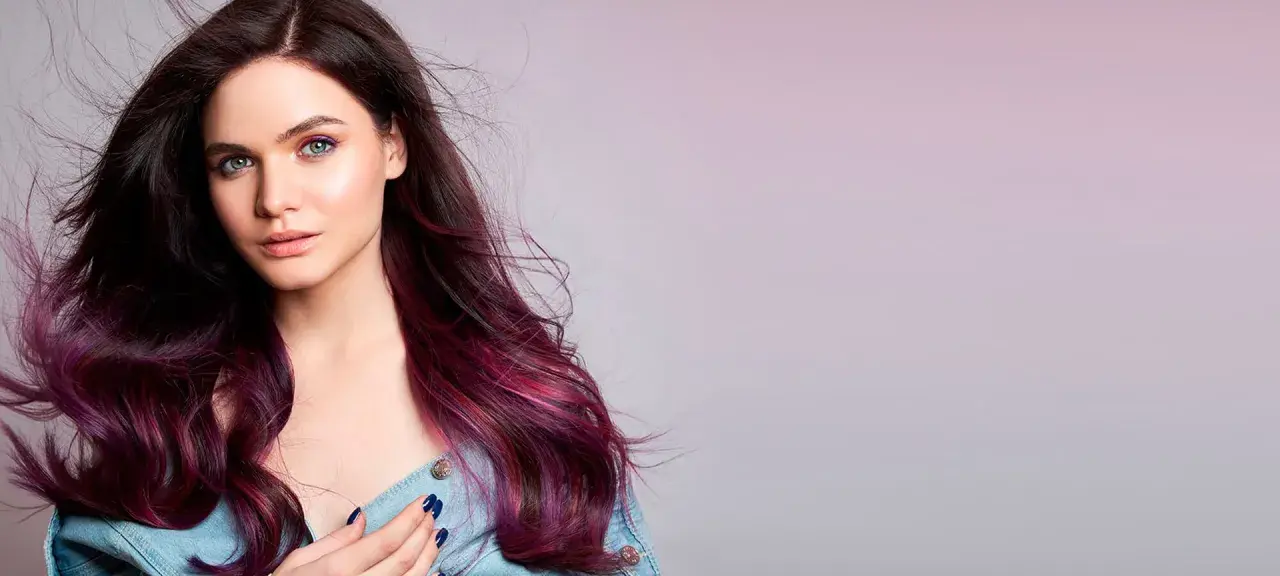 Modella con capelli viola prugna scuro che sfumano in tonalità più chiare, occhi verdi e trucco audace.