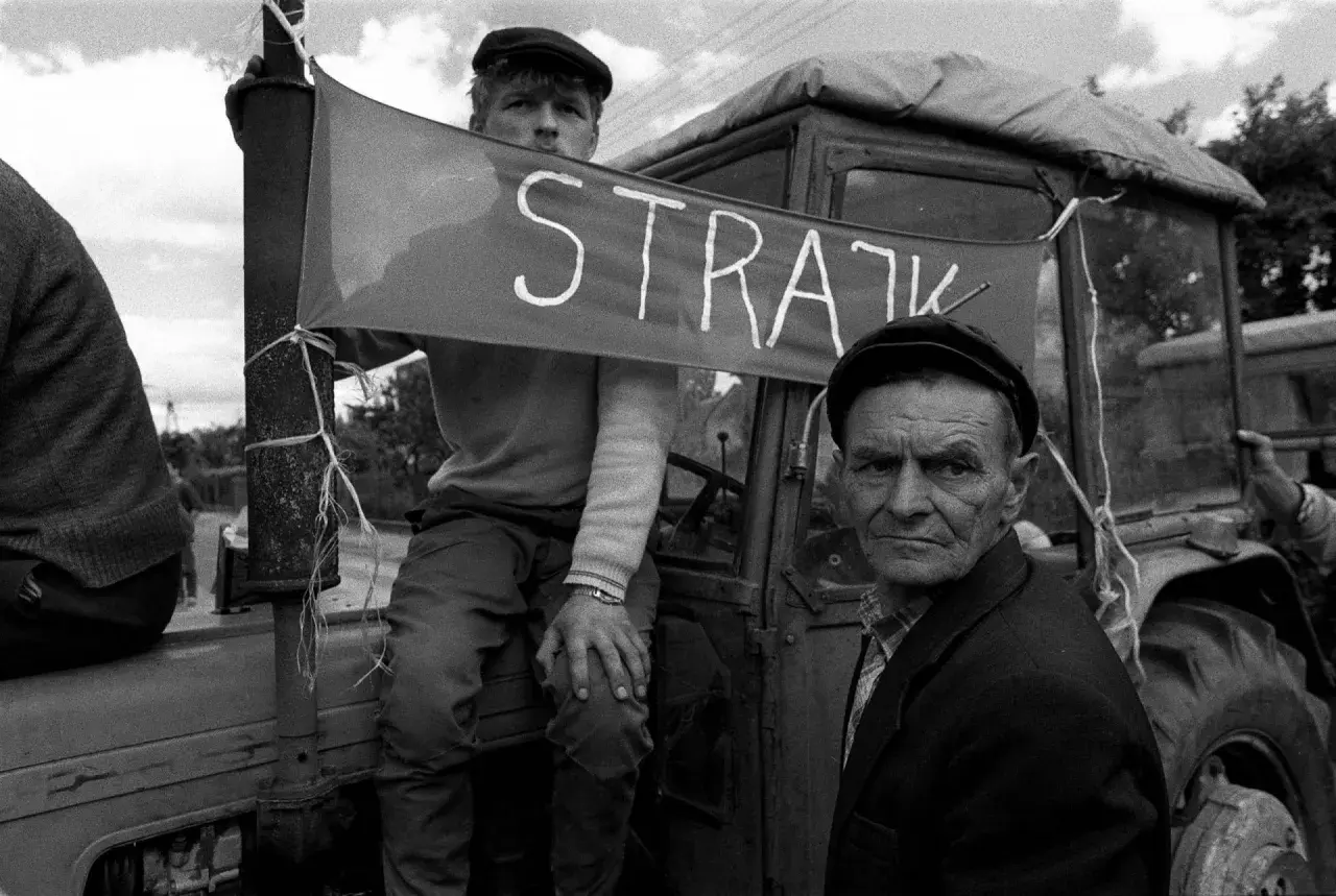 Dwóch mężczyzn w czapkach na tle traktora z banerem "STRAJK".