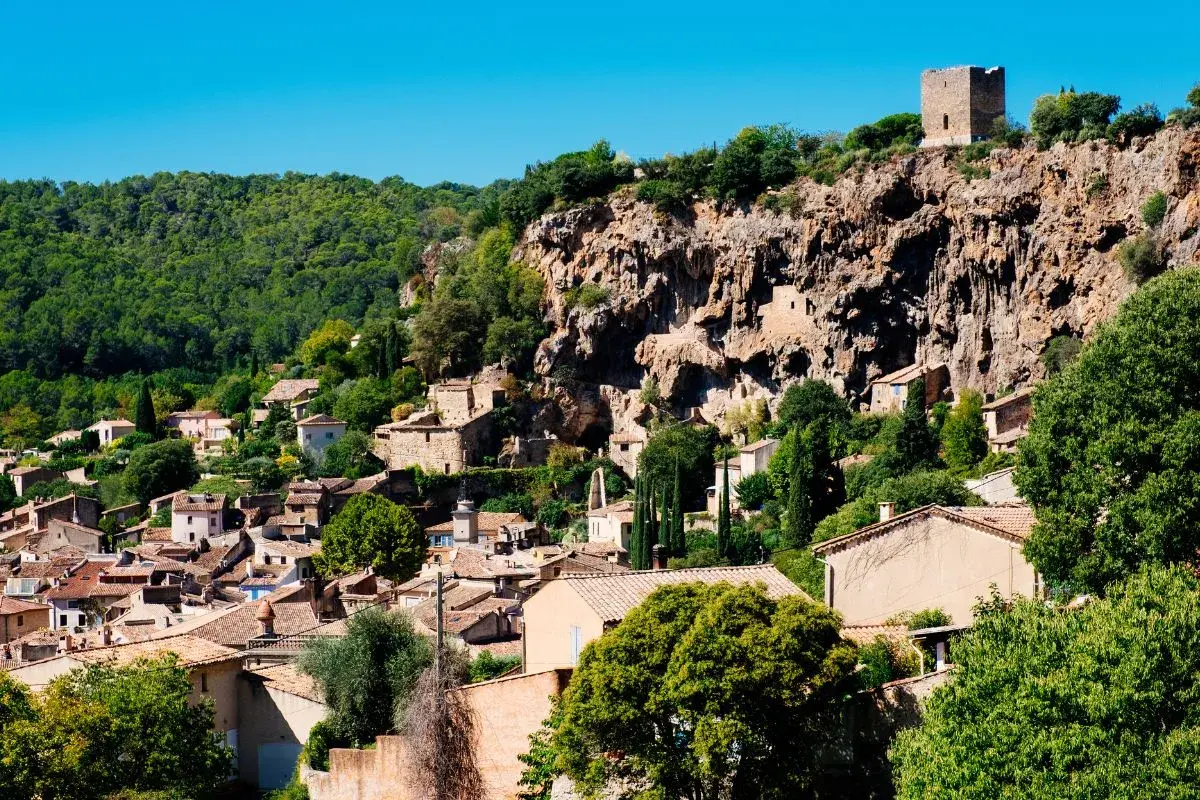 Vue d'un village perché du Var, accroché à une falaise rocheuse, avec des maisons aux toits de tuiles et une tour médiévale.