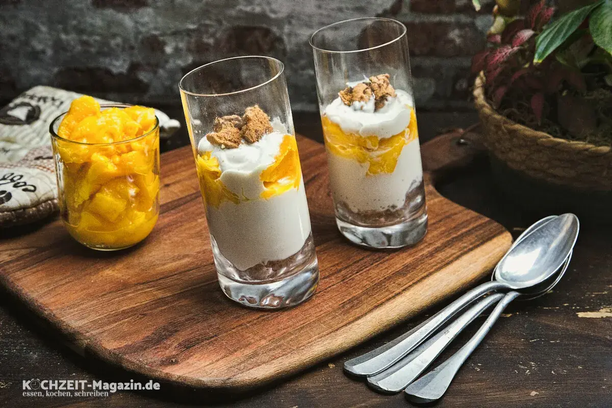 Zwei Gläser mit Mango-Creme und Kekskrümeln, daneben ein Glas mit Mangostücken. Perfekt für leichte ricotta rezepte.