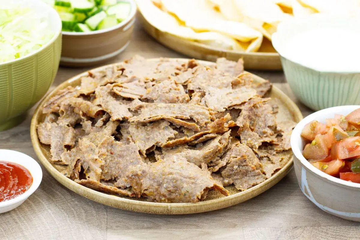 Pyszny kebab z piekarnika na talerzu, otoczony świeżymi warzywami, sosem i plackami. Idealny na domowy obiad.
